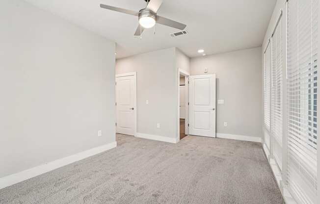 A large bedroom with floor to ceiling windows all through out the room, carpeted floor, a ceiling fan