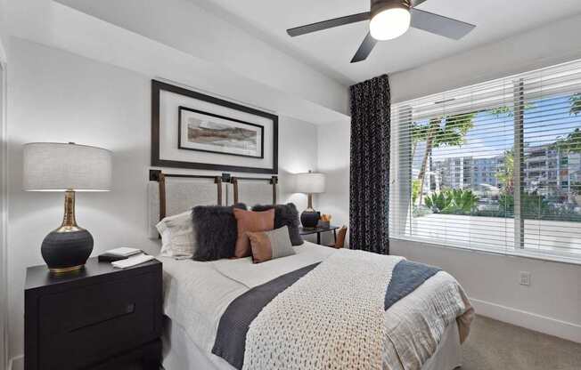 A bedroom with a large bed, a ceiling fan, and a window with blinds.