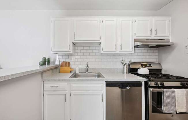 A white kitchen with a stove, sink, and cabinets.