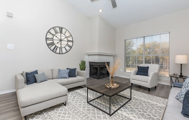 A living room with a fireplace, a couch, a chair, and a clock on the wall.