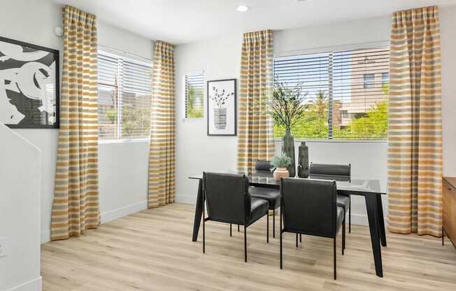a dining room with a table and chairs and windows with yellow curtains