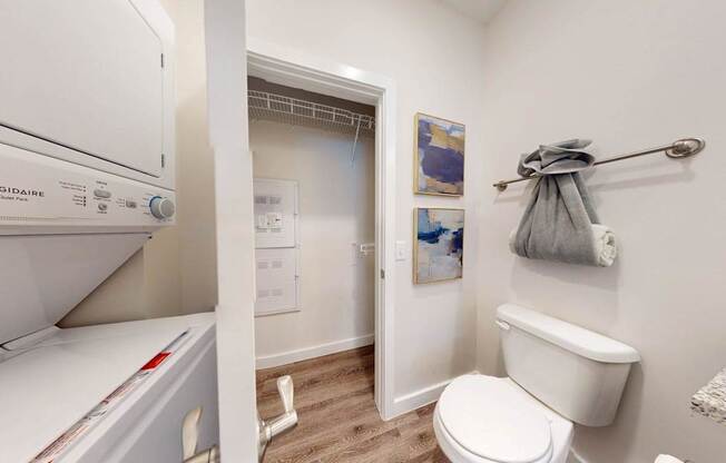 A white dryer is on the left of a white toilet in a small bathroom.