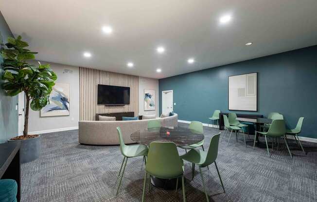 A room with a grey carpet and a round table with green chairs.