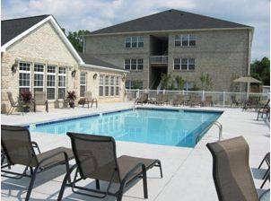 A pool surrounded by chairs in front of a house.