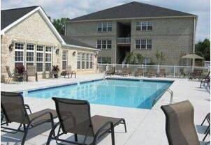 A pool surrounded by chairs in front of a house.