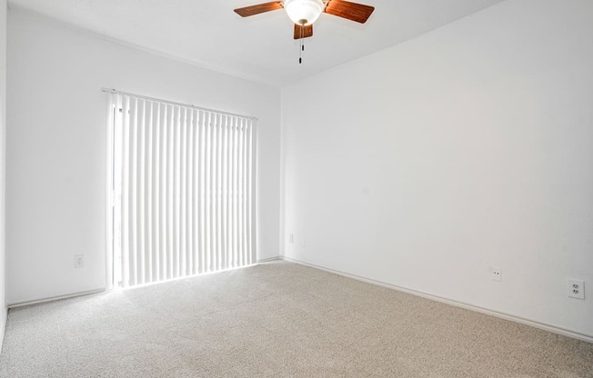 an empty living room with blinds and a ceiling fan