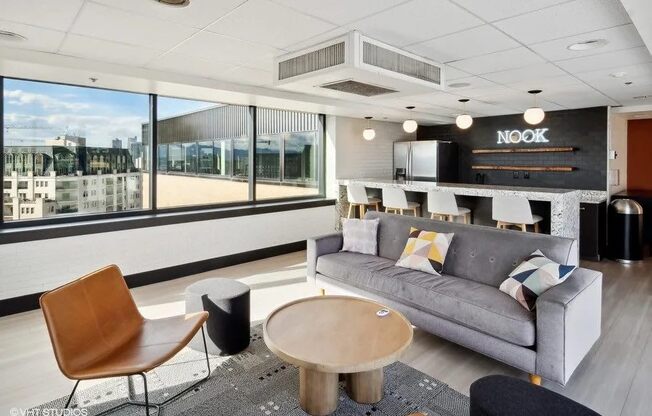 A modern living room with a grey sofa, a wooden chair, and a coffee table at Archer Tower in Denver, CO