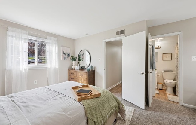 A bedroom with a bed, nightstand, and a bathroom visible through the open door.