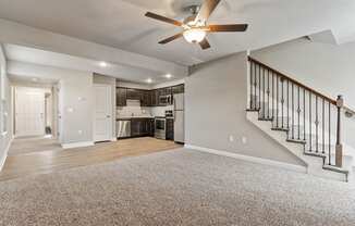 an empty living room with a ceiling fan and a kitchen