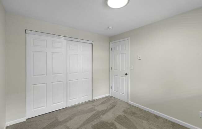 a bedroom with two closet doors and a carpeted floor at Swiss Gables Apartment Homes, Kent, 98032