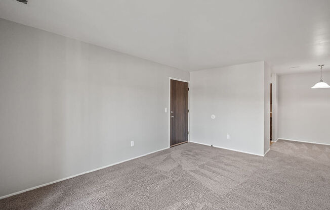 an empty living room with carpet and a door to a bedroom
