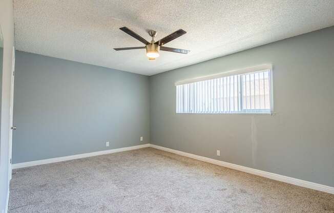 A room with a ceiling fan and a window with blinds.