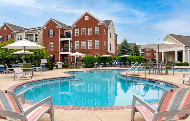 A pool surrounded by chairs and umbrellas in front of a brick building.