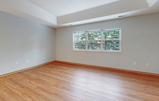 A room with wooden flooring and a window with a view of trees.