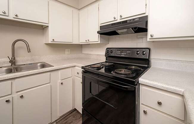 A black stove in a kitchen with white cabinets.