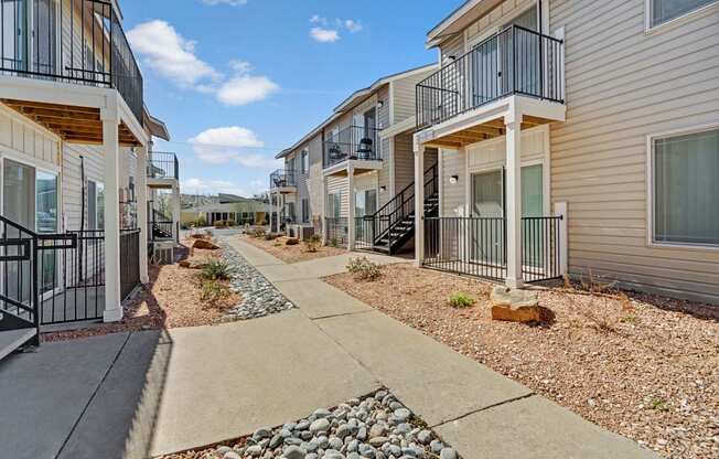 A sunny exterior walkway at Acacia Park featuring private balconies and patios, clean concrete paths, low-maintenance landscaping, and a welcoming layout that makes moving around the community easy and comfortable.