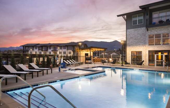 a swimming pool at dusk with a building and mountains in the background