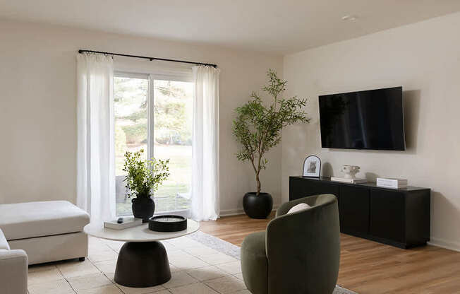 A living room with a green chair, a white sofa, a black table, and a flat screen TV mounted on the wall.