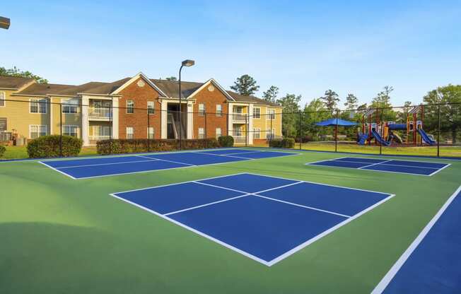 a blue and green tennis court with yellow apartments in the background