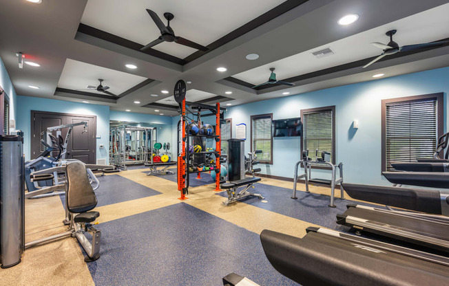 a gym with weights and cardio equipment on the floor and a blue wall