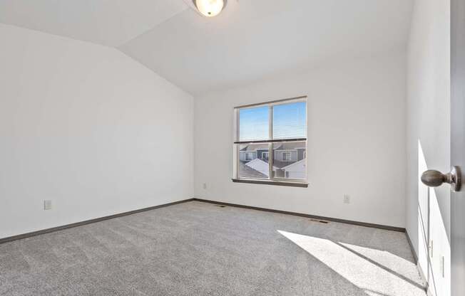A room with a carpeted floor and a window showing a house view.