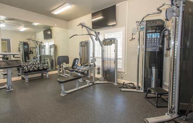 A gym with a variety of equipment including a squat rack, a bench, and a barbell at Stoneridge Apartments, California, 95661