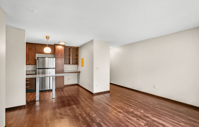 an empty living room and kitchen with wood flooring and white walls