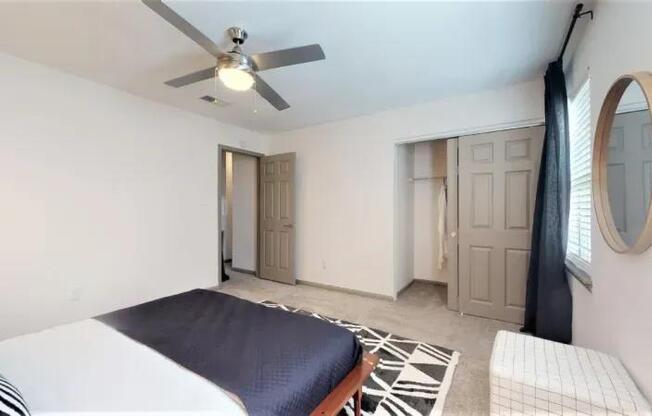 A bedroom with a bed, a ceiling fan, and a mirror.