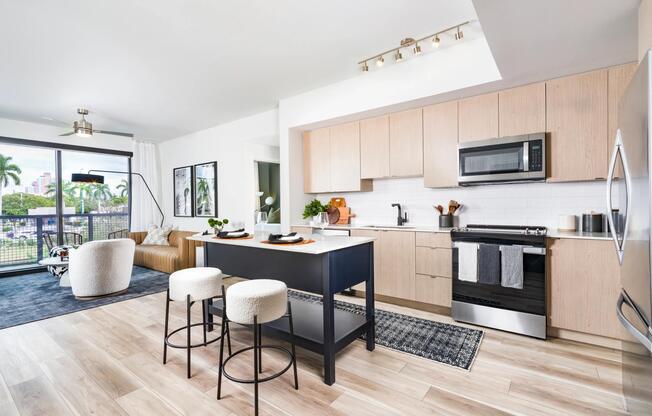 Light-filled kitchen design pairs warm wood cabinetry with a sculptural island, flowing seamlessly into open living spaces at Modera Aventura.