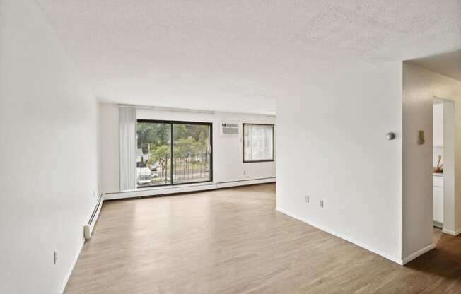 the living room and dining room of an apartment with wood floors and a large window