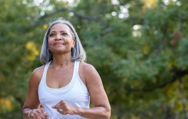A woman in a white tank top is running outdoors.