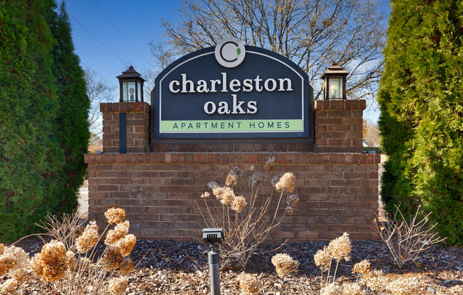A sign for Charleston Oaks Apartment Homes is displayed in front of a brick wall.
