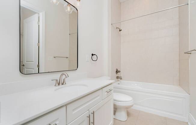 a bathroom with white cabinets and a white toilet next to a white bathtub with a shower