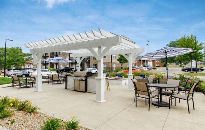 A white pergola with black chairs and tables is set up in a sunny outdoor area.