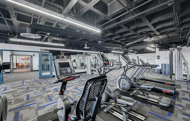 A gym with a variety of exercise equipment including treadmills, stationary bikes, and elliptical machines.