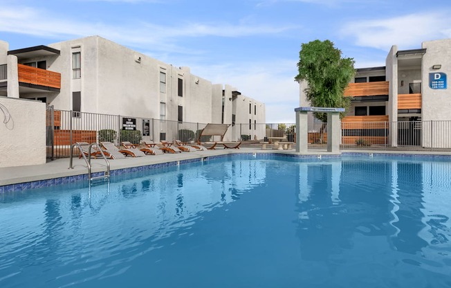 a large swimming pool with lounge chairs and a building in the background