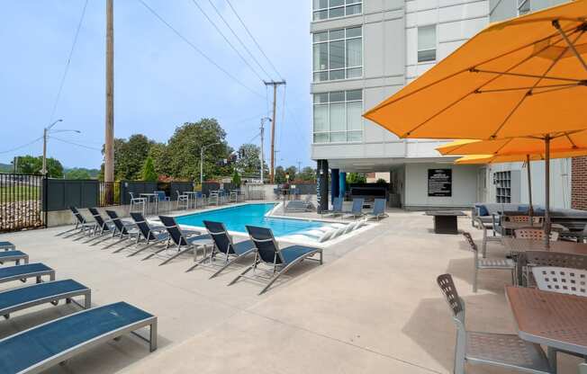 a swimming pool with chaise lounge chairs and umbrellas in front of a building