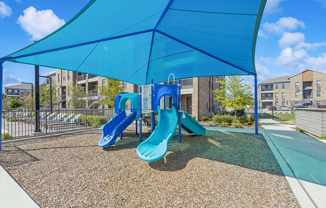 Community Playground with Slides and Blue Canopy at Alta 3Eighty Apartments located in Aubrey, TX.