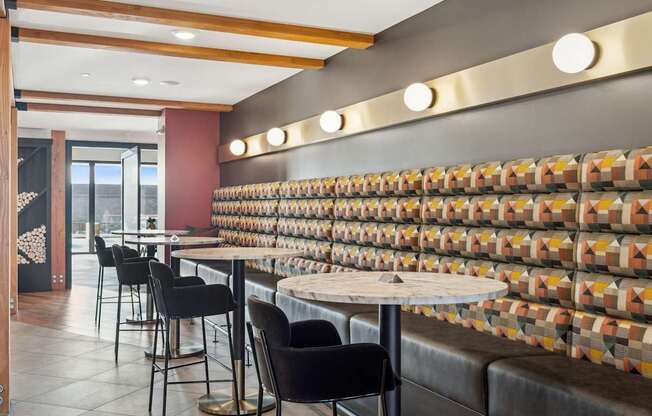 A restaurant with a long table and chairs with a wall of tiles behind it.