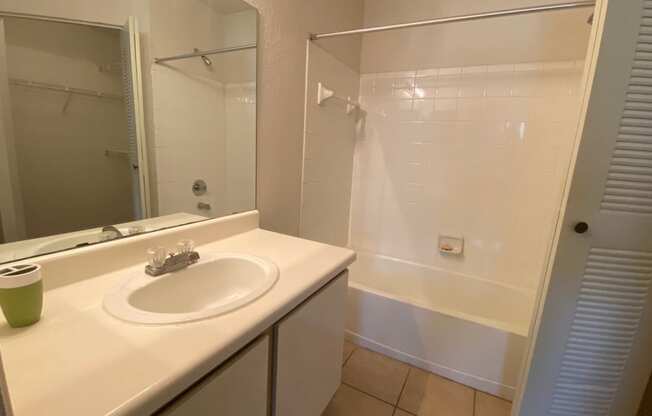 Bathroom with tile floors, toilet, shower tub combo with tile back splash, towel bar, white cabinets and large mirror