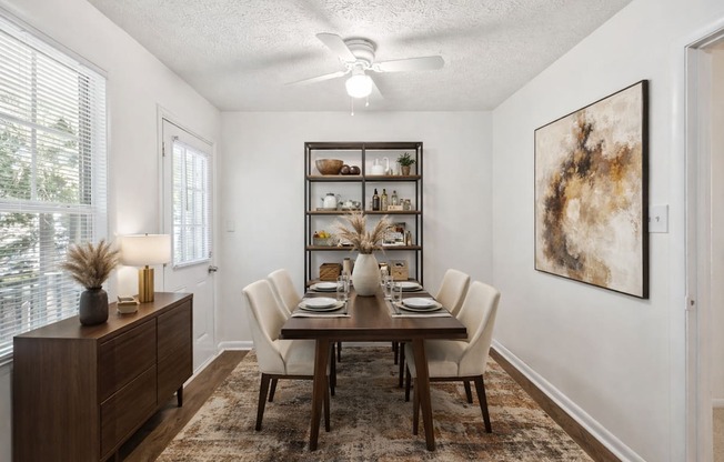 A dining room with a table set for six and a painting on the wall.