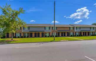 A building with a grey roof and black windows is surrounded by a grassy area and a clear blue sky.