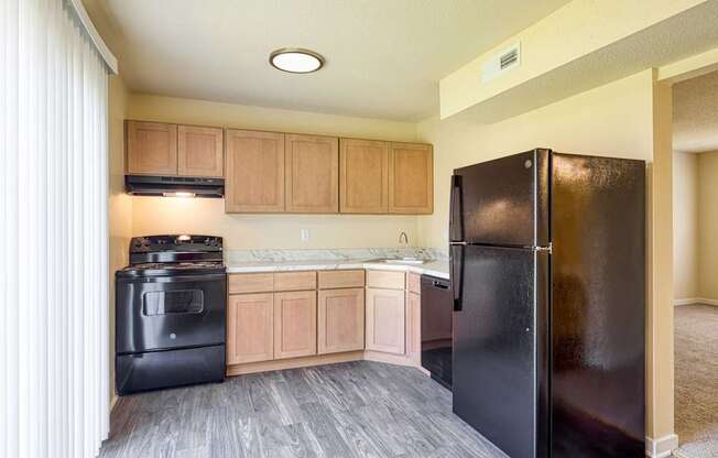 A black refrigerator is in a kitchen with wooden cabinets.