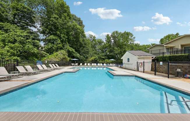 A large swimming pool surrounded by trees and lounge chairs at Gwinnett Square Apartments in Duluth, GA
