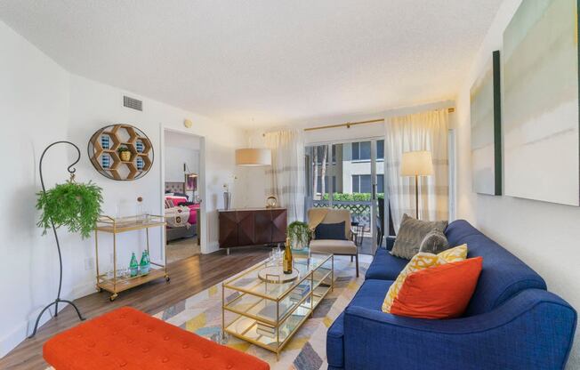 Living room with patterned area rug and colorful couch, chair, and ottoman, coffee table, and balcony door