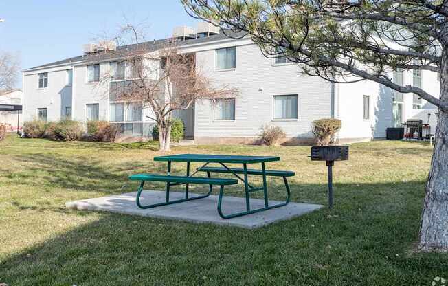 A green picnic table sits in front of a grey building.