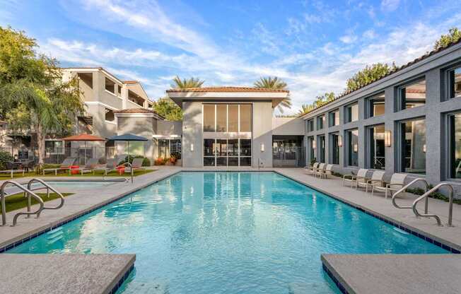 A large swimming pool in front of a building with lounge chairs around it.