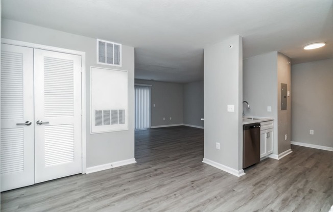 an empty living room with white doors and a kitchen