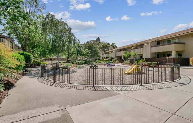 a fenced in play area with a playground in front of a building at Summerwood Apartments, Santa Clara, California