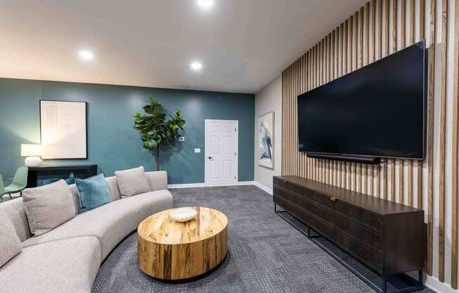 A modern living room with a grey sofa, a wooden coffee table, and a flat screen TV mounted on a wooden wall.